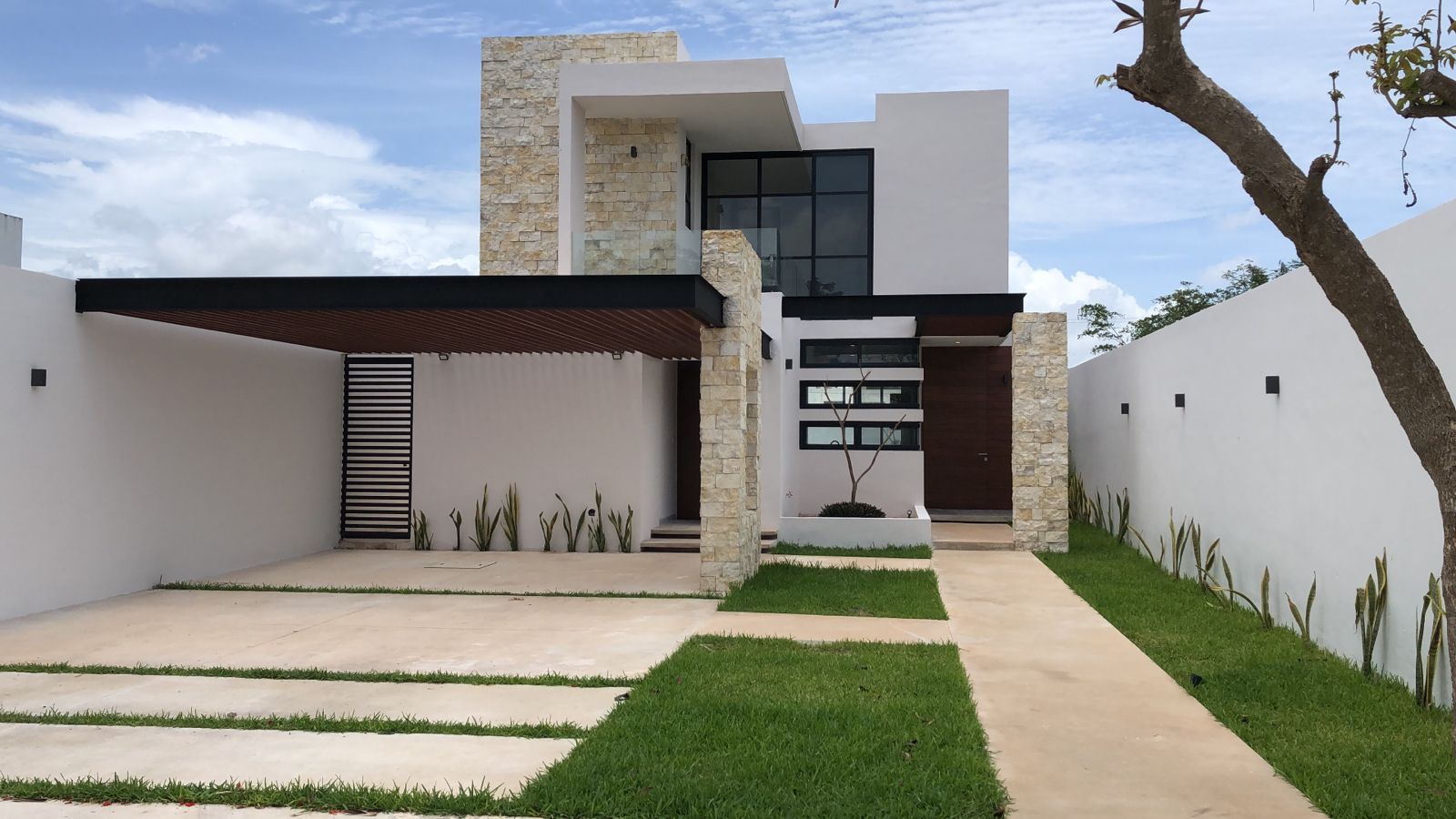 Arbórea 290 terminada: volumen de piedra crema maya, cancelería negra y pérgola sobre el jardín